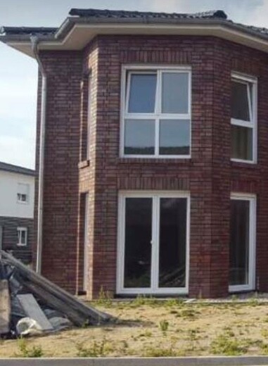 Aussenansicht eines roten Ziegelhauses mit grossen Fenstern auf Baufläche