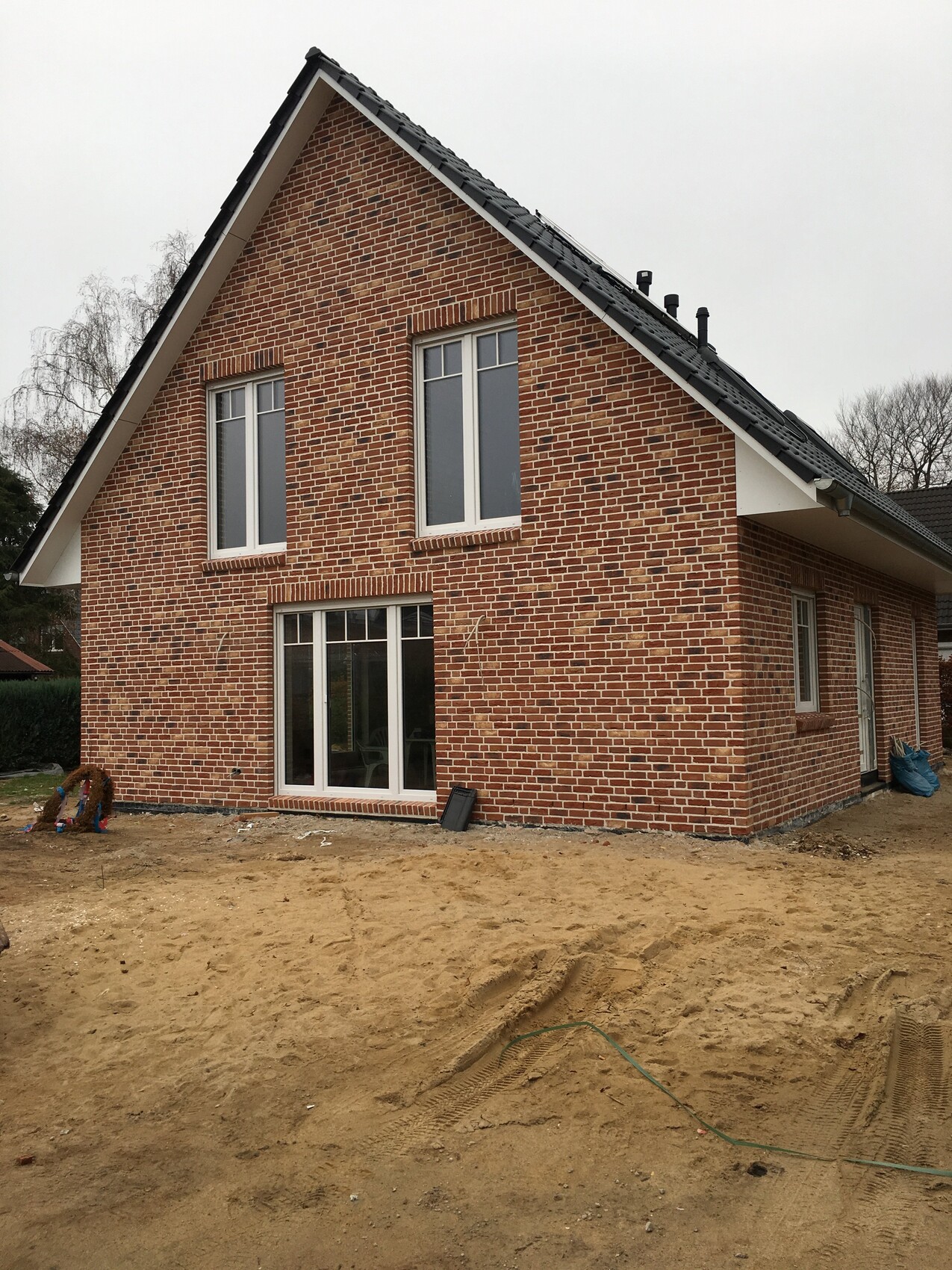 Ziegelhaus mit Satteldach, zwei Fenster oben und große Glastür unten; Sandboden.