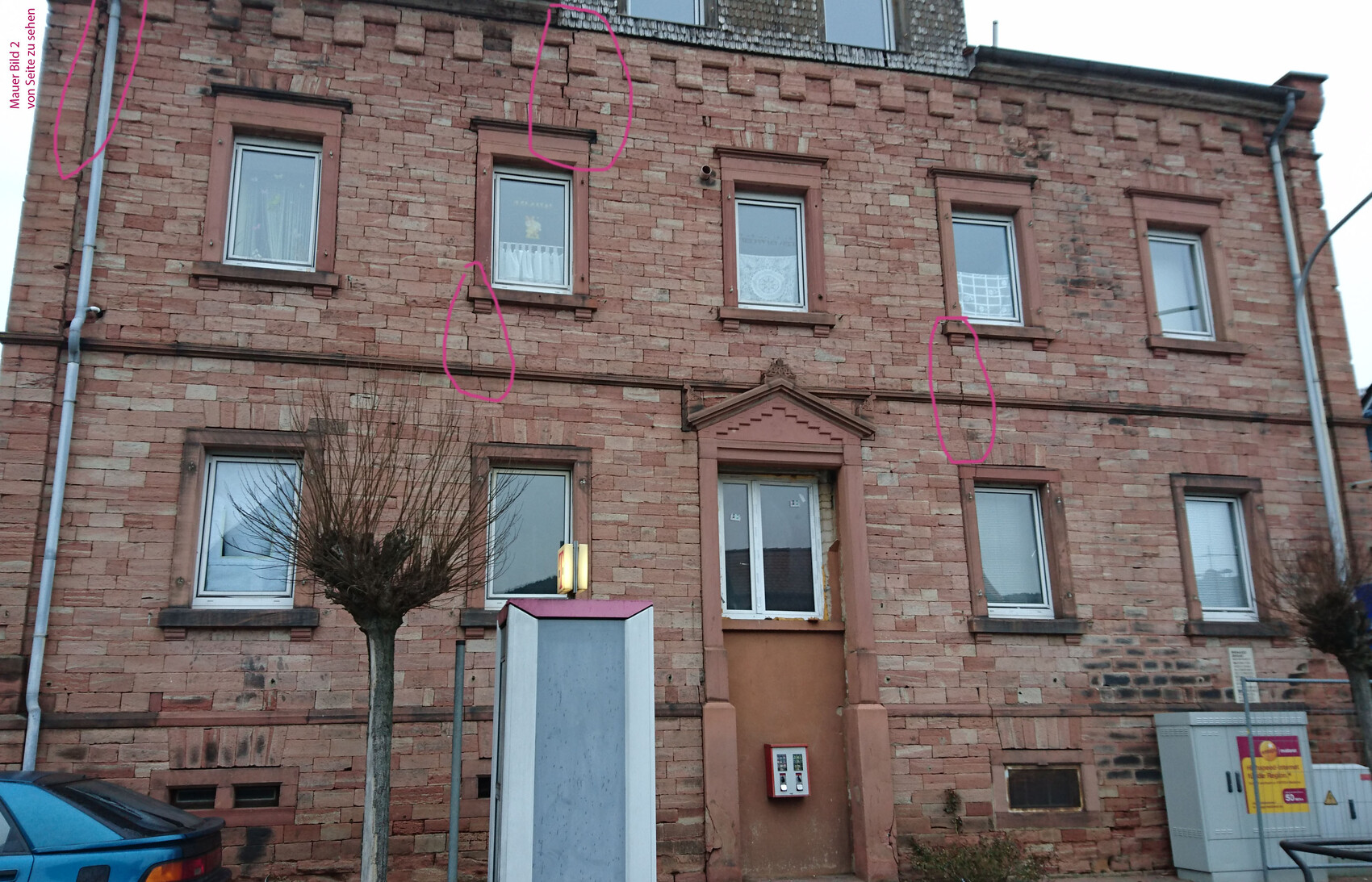 Rotes Backsteingebäude mit Fenstern, Eingang, Baum davor; Fassadenrisse markiert.