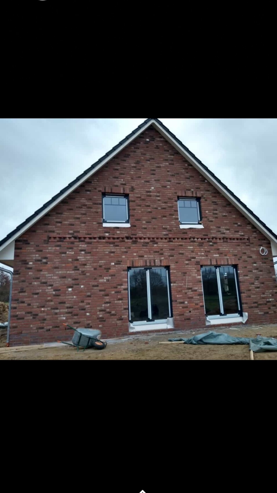 Neues rotes Ziegelhaus mit Satteldach; zwei Oberfenster und große Glasfront vorne, Baugerät davor.