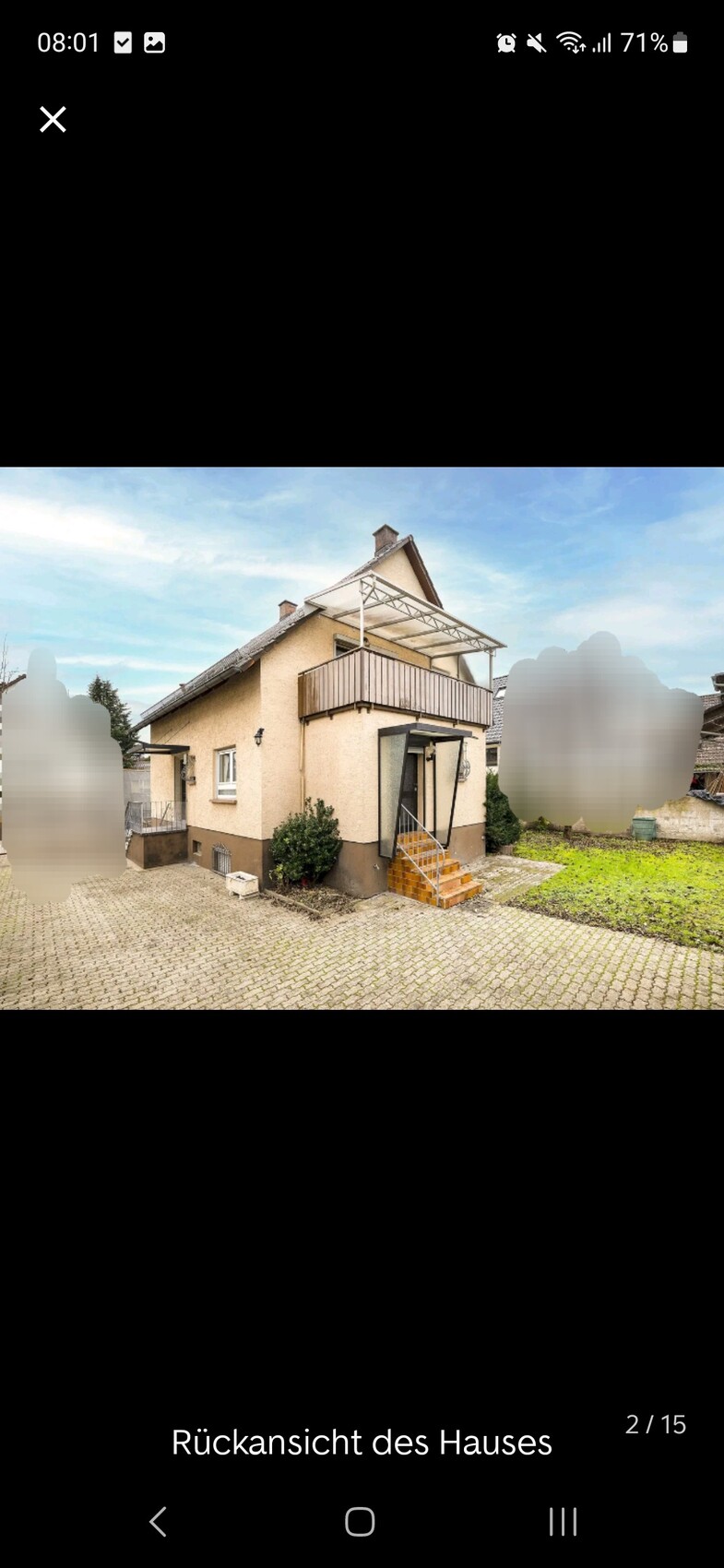 Rückansicht eines zweistöckigen, beige verputzten Hauses mit Balkon und Treppenaufgang.