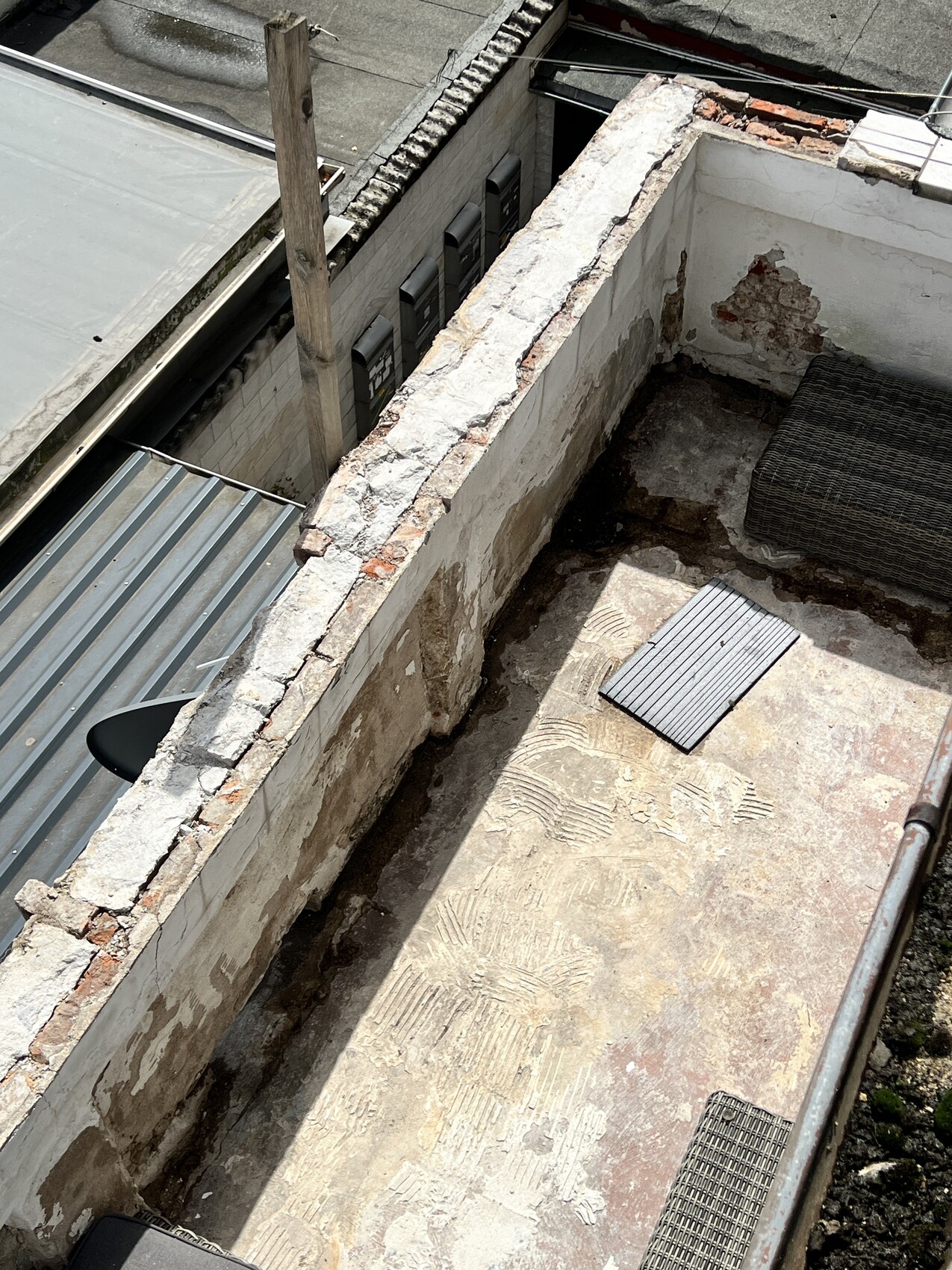 Verwitterte Dachterrasse mit freigelegten Ziegeln, bröckelndem Putz und Korbsessel.