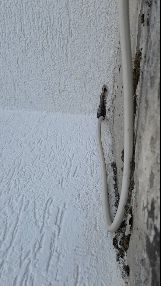 Weiße, strukturierte Wand mit einem weißen Kabel, das durch ein Loch tritt und hängt herab.