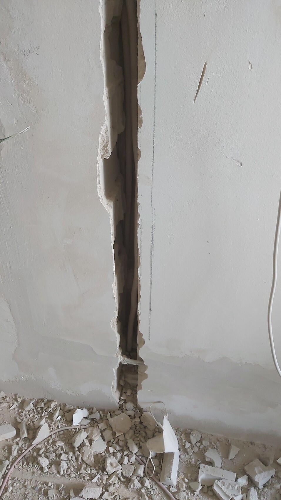 Senkrechter Riss in der Wand mit freiliegter Rohrleitung Trümmer und Kabelreste liegen auf dem Boden.