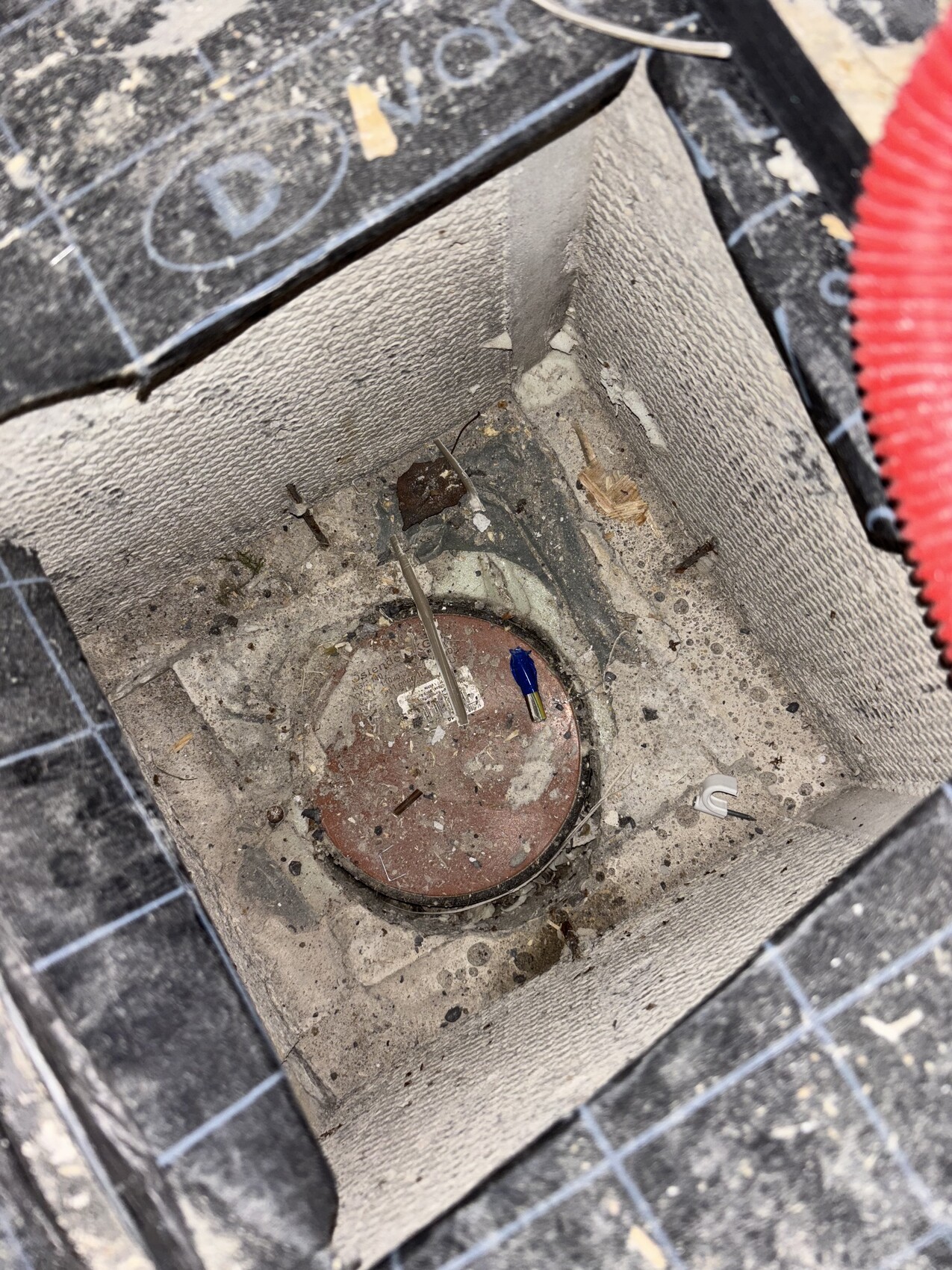 Offener Installationsschacht im Boden mit rotem runden Deckel, Staub und Kabelreste.