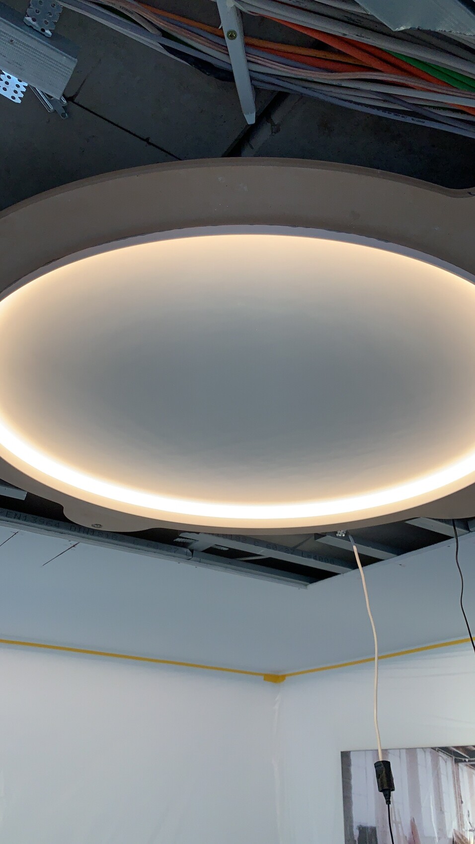 Runde LED-Deckenleuchte mit hellem Lichtkranz; Bau-/Werkstattraum mit sichtbaren Kabeln im Hintergrund.