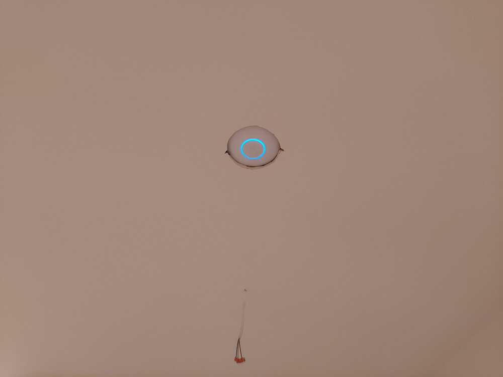 Runde weiße Deckenplatte mit blauem Ringlicht; darunter hängt loses Kabel.