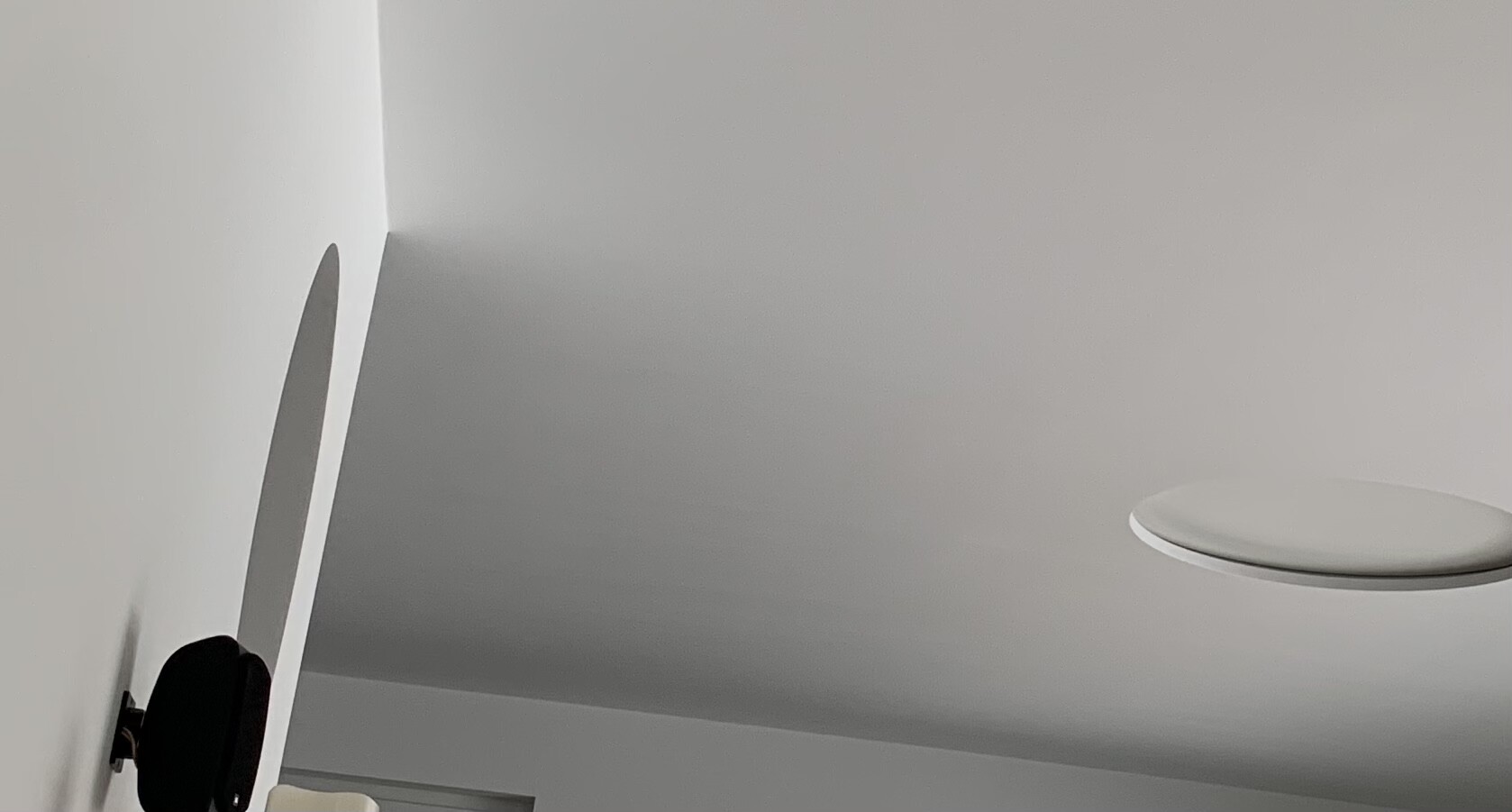 Weißer Innenraum mit runder, flacher Deckenleuchte rechts; linke Wand sichtbar.