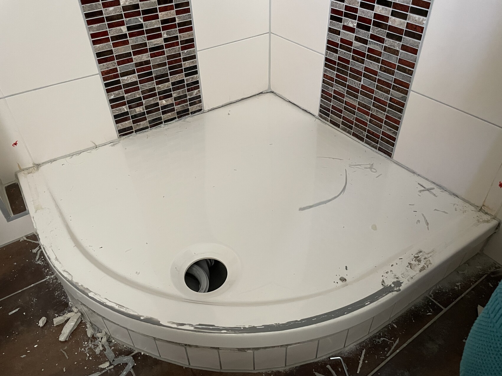 Halbrunde Duschwanne mit weißem Boden, zentralem Abfluss, weiße Wandfliesen und rote Mosaikfliesen.