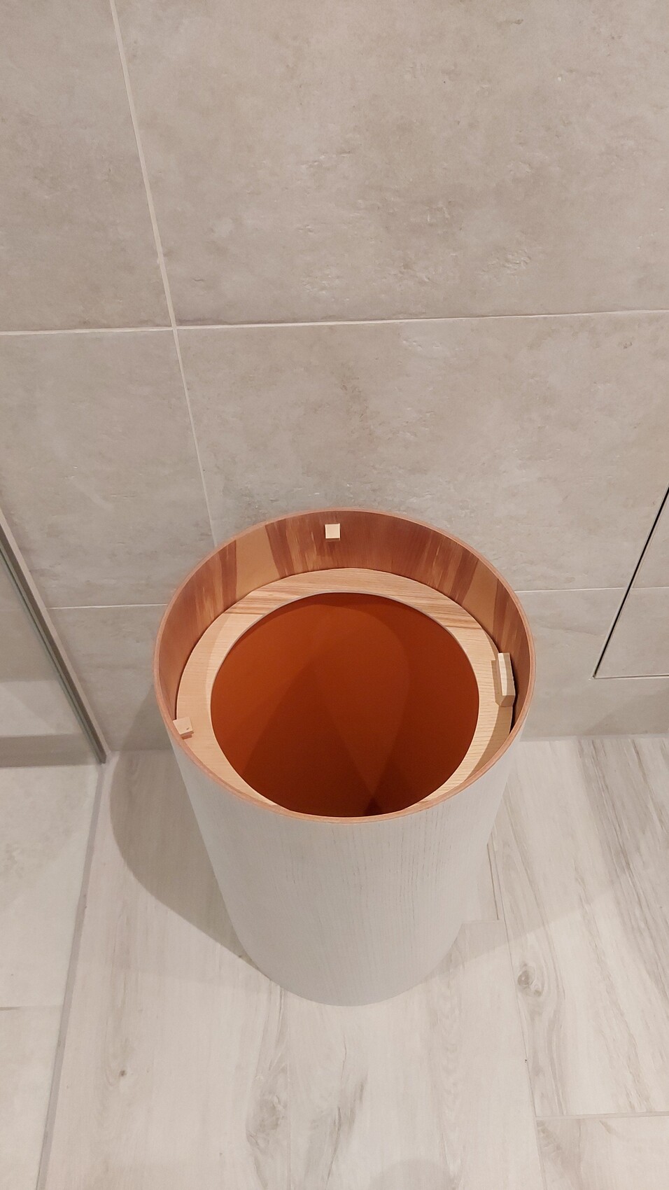 Offener runder Holzbehälter (Eimer) mit orangefarbener Innenfläche im Badezimmer.