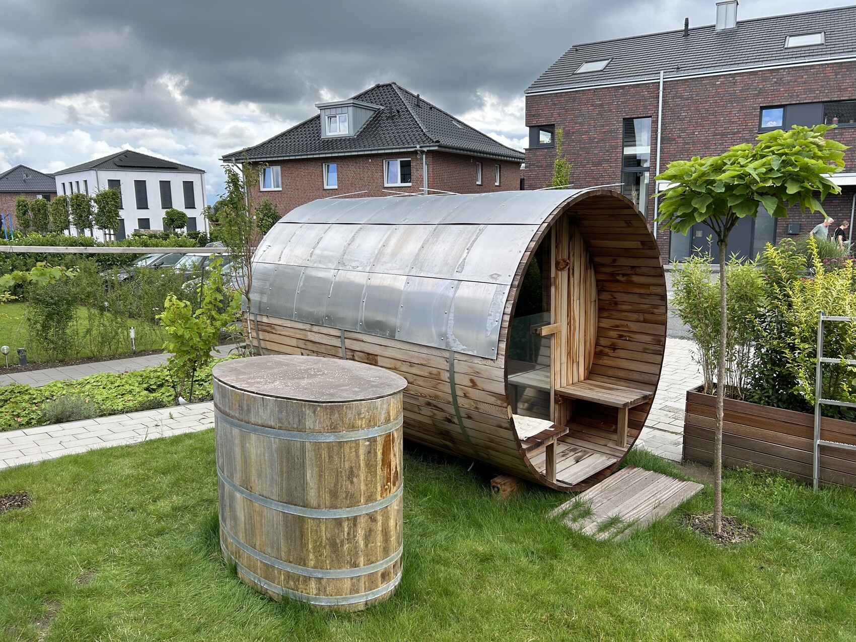 Runde Holzsauna im Garten, Barrel-Form mit Metall-Dach, Eingang und Holzbänken.