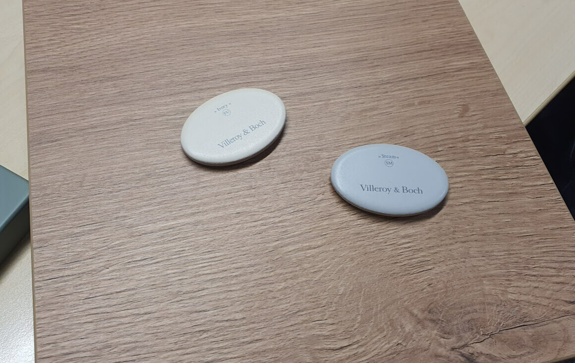 Zwei ovale, hellgraue Untersetzer mit dem Logo Villeroy & Boch auf einer Holzoberfläche.