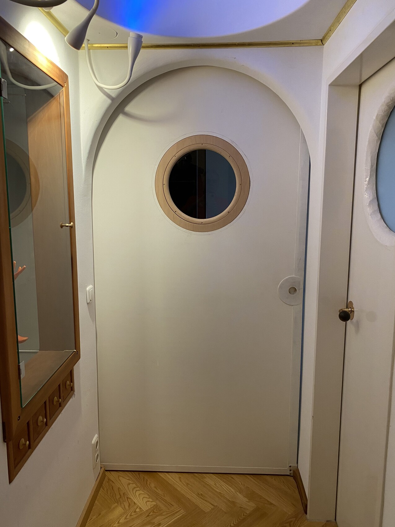 Weiße Tür mit rundem Bullaugenfenster im Innenflur, linker Spiegelkasten, Holzboden.