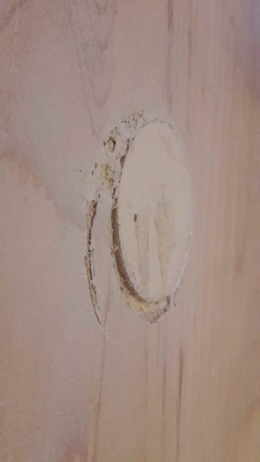 Nahaufnahme von einem runden Bohrloch in Holzplatte mit rauen Kanten.