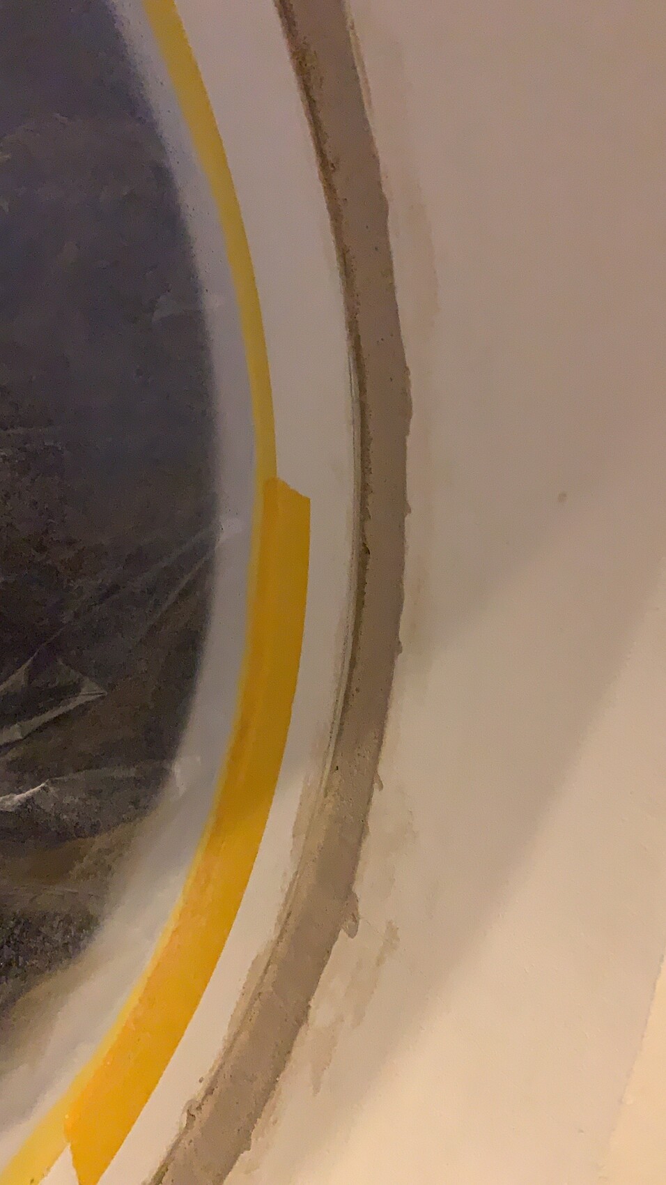 Rundes Fenster in weißer Wand, gelber Rand und dunkler Innenraum.
