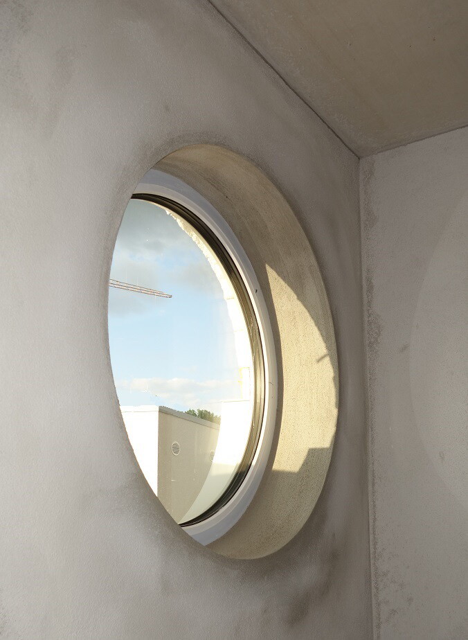 Rundes Fenster in einer hellen Innenwand; Blick nach draußen auf Gebäude und Baukran.