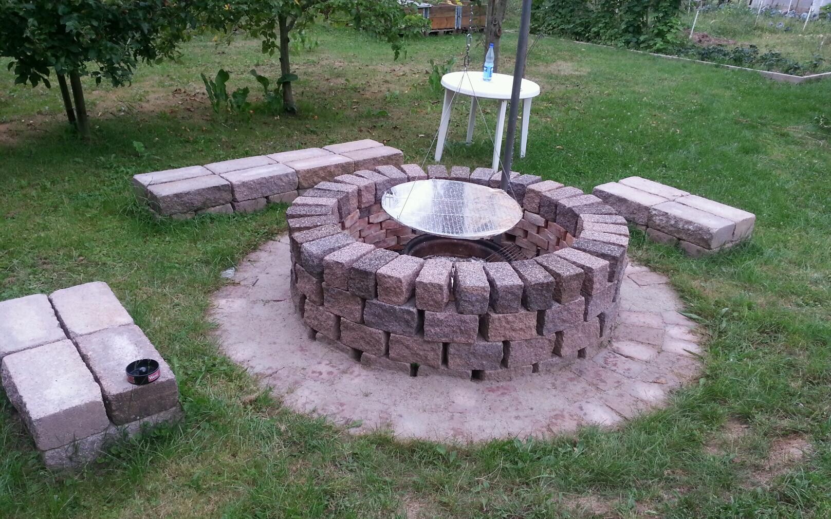 Runde Feuerstelle aus Bruchstein mit Metallabdeckung, umlaufende Sitzsteine.