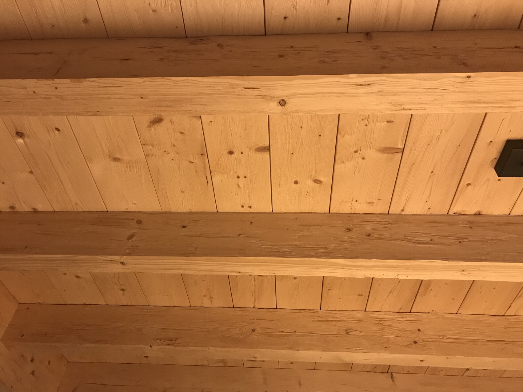 Holzdecke mit Balken, warme Beleuchtung, rustikale Holzbretter.
