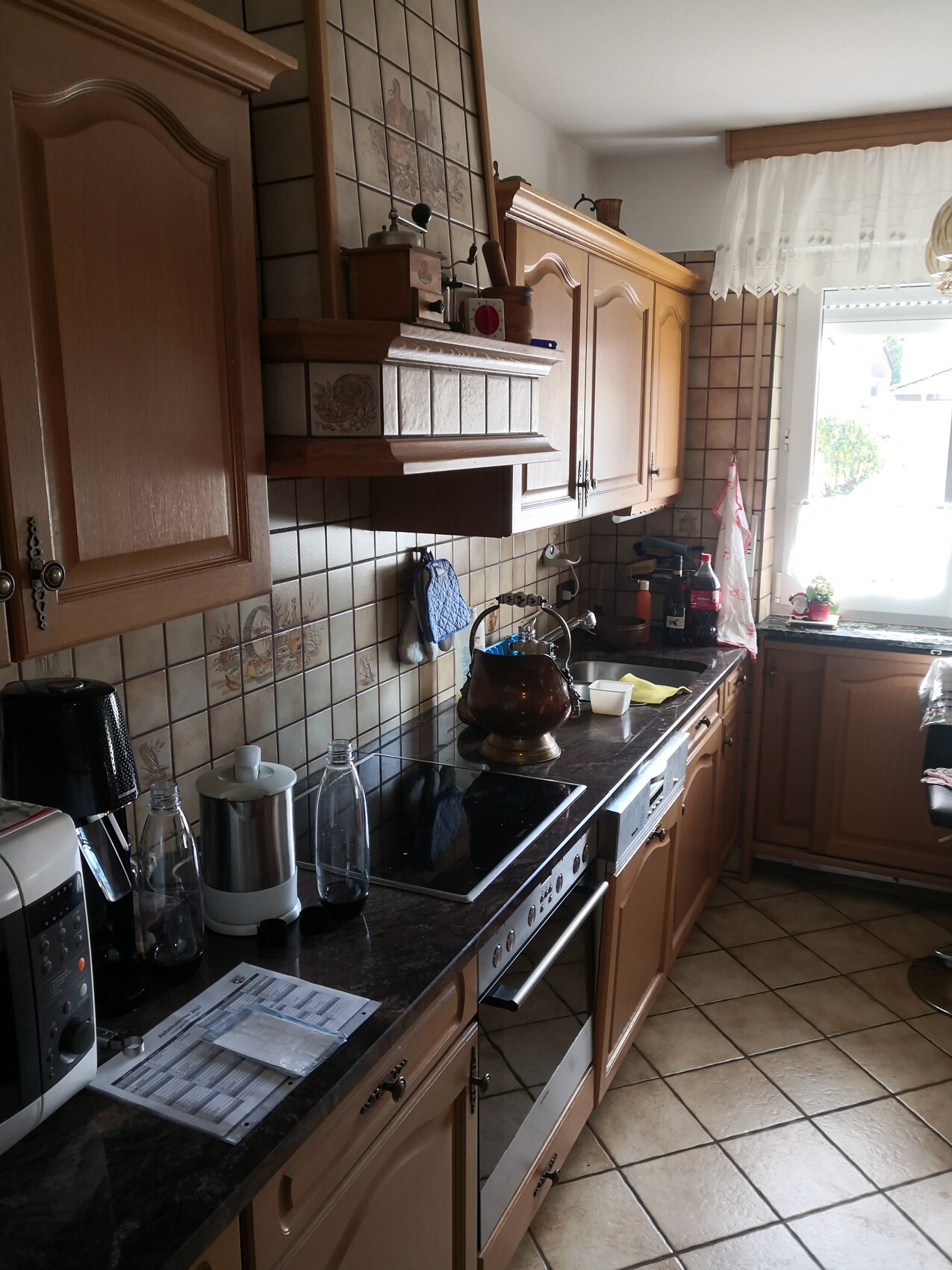 Küche mit braunen Holzschränken, Herd mit Glaskeramik, Spüle, Dunstabzug, Fenster rechts.