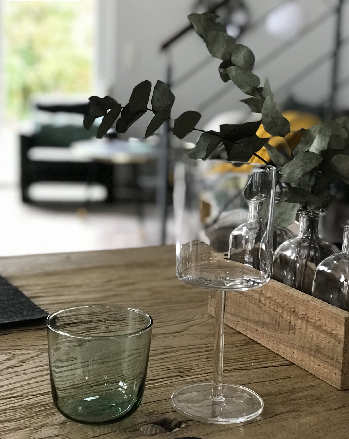Rustikaler Holztisch mit Weinglas, grünem Glas und Eukalyptus im Wohnzimmer