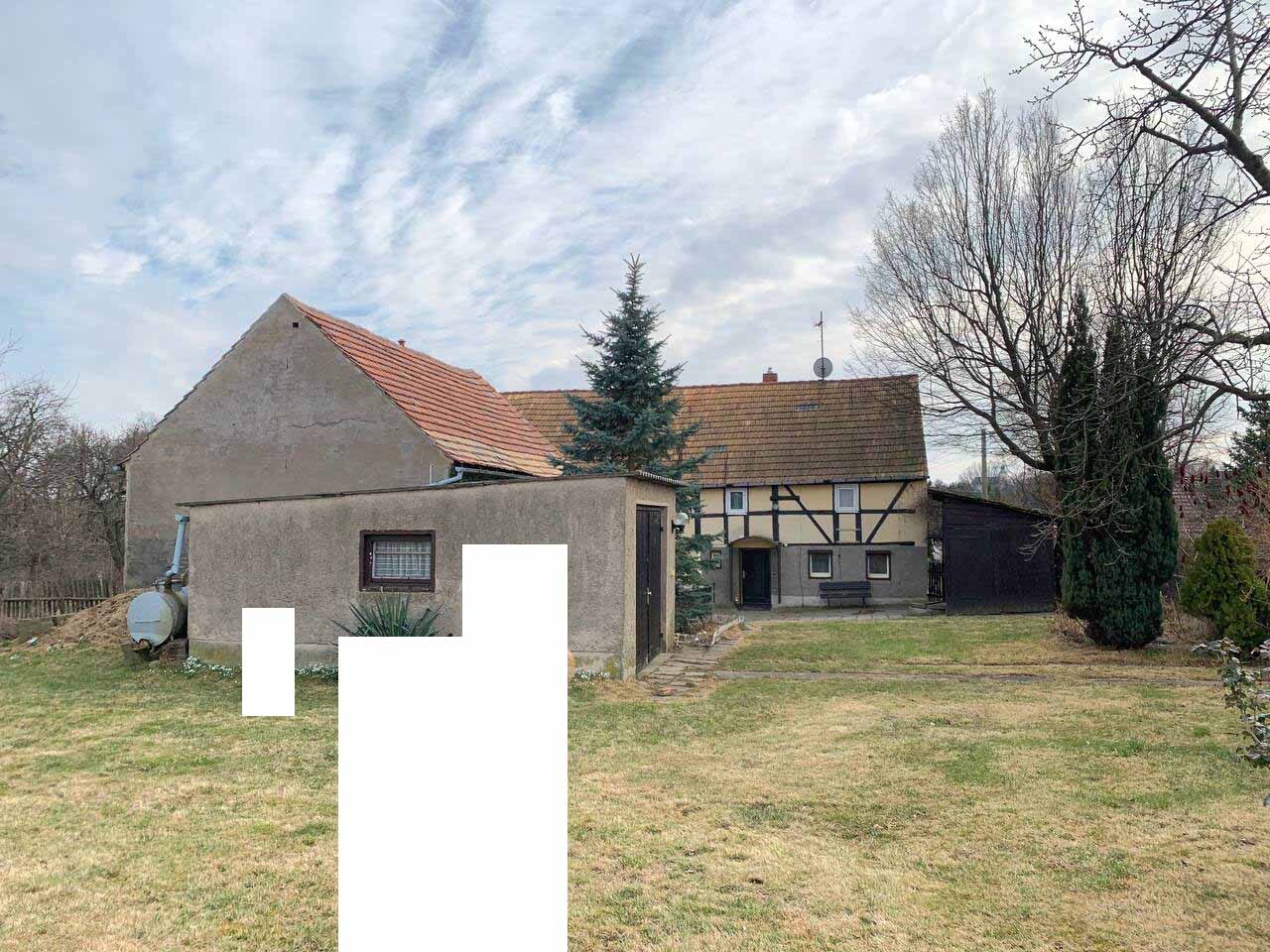 Hofansicht mit zwei Häusern: links Putzhaus, rechts Fachwerkhaus, Nadelbaum, kahle Bäume, Rasen.
