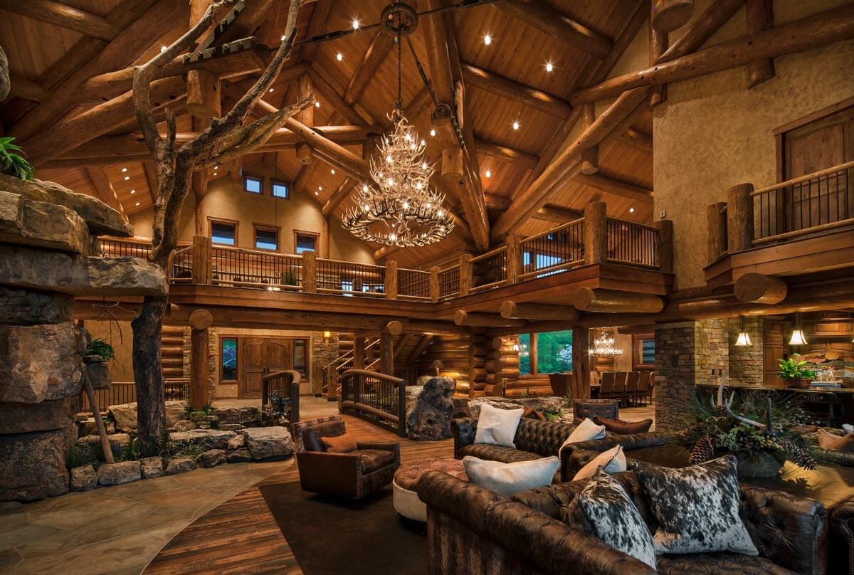 Großes rustikales Wohnzimmer im Holzhaus mit Deckenbalken, Ledersofas und Kronleuchter