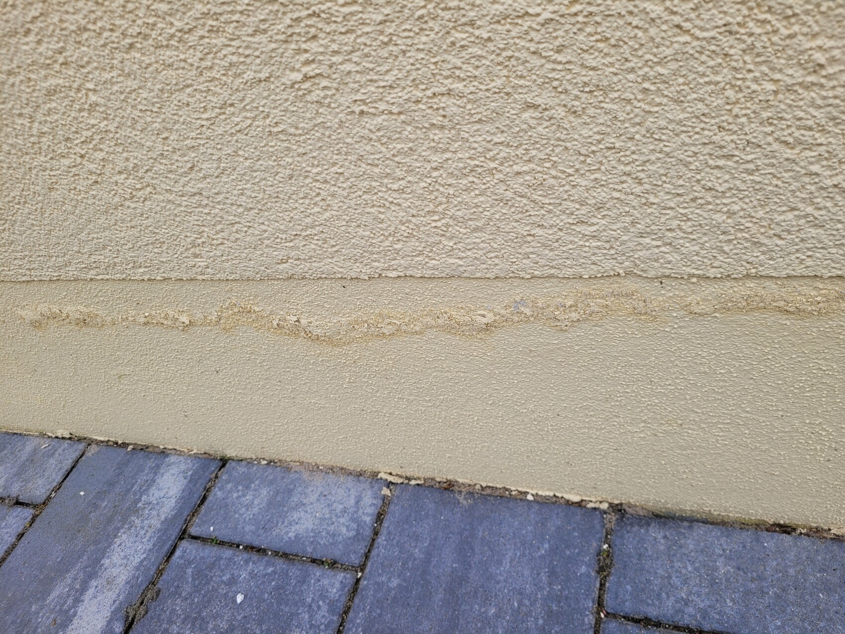 Außenwand mit rauer Putzoberfläche, Sockelbereich und blau-graue Pflastersteine.