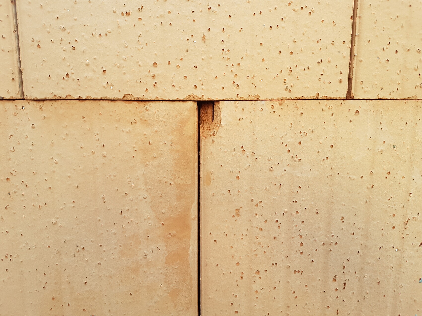 Nahaufnahme von vier sandfarbenen Steinblöcken mit vielen Poren und einer Fuge in der Mitte.