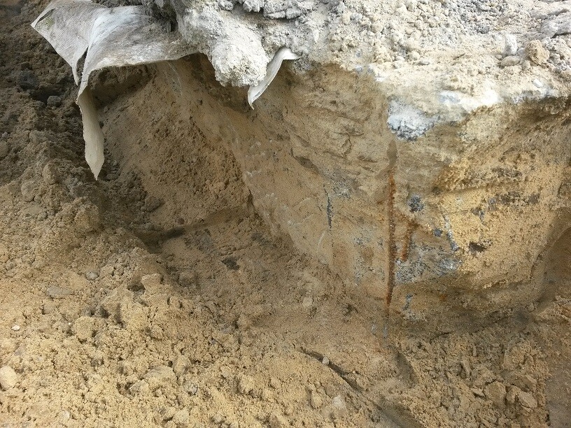 Baugrube mit sandigem Aushub und Baufolie am Rand einer Baustelle