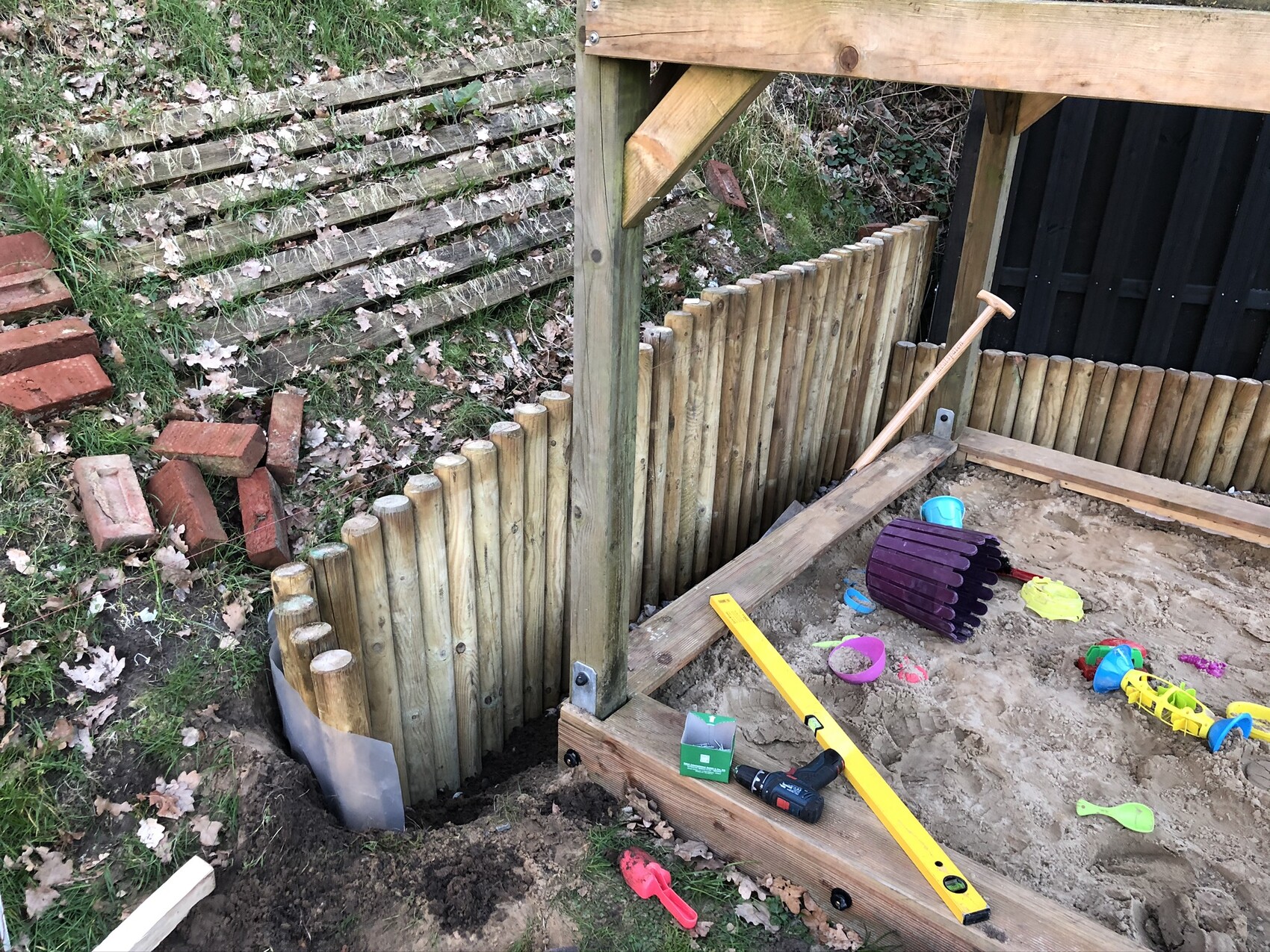 Garten-Sandkasten mit Holzwand aus Palisaden, Spielzeug und Werkzeugen.