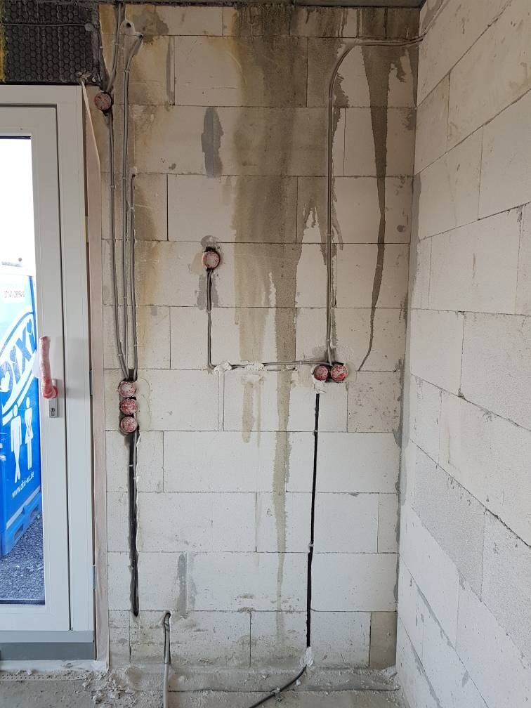 Innenwand aus weißen Porenbetonblöcken mit sichtbaren Leitungen, Rohren und Feuchtigkeitsspuren.