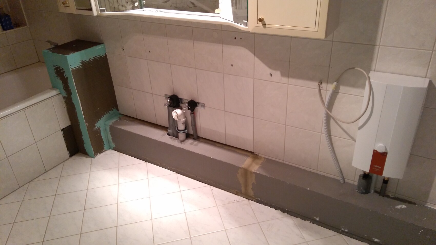 Badezimmer mit sichtbaren Sanitärrohren, Heizgerät und Renovierungsarbeiten an der Wand.