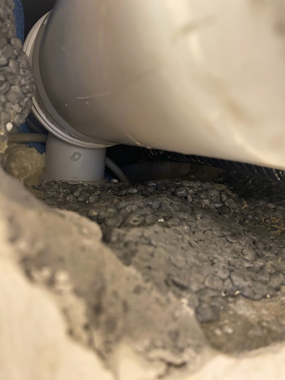 Nahaufnahme eines grauen PVC-Rohrs mit 90-Grad-Bogen in einer Baugrube, umgeben von Kies.