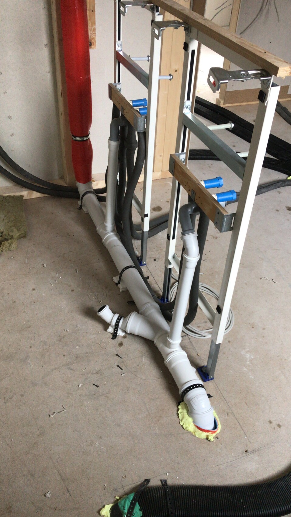 Unterbau mit offenen Abflussrohren, PVC-Rohren, schwarzen Schläuchen und Metallrahmen.
