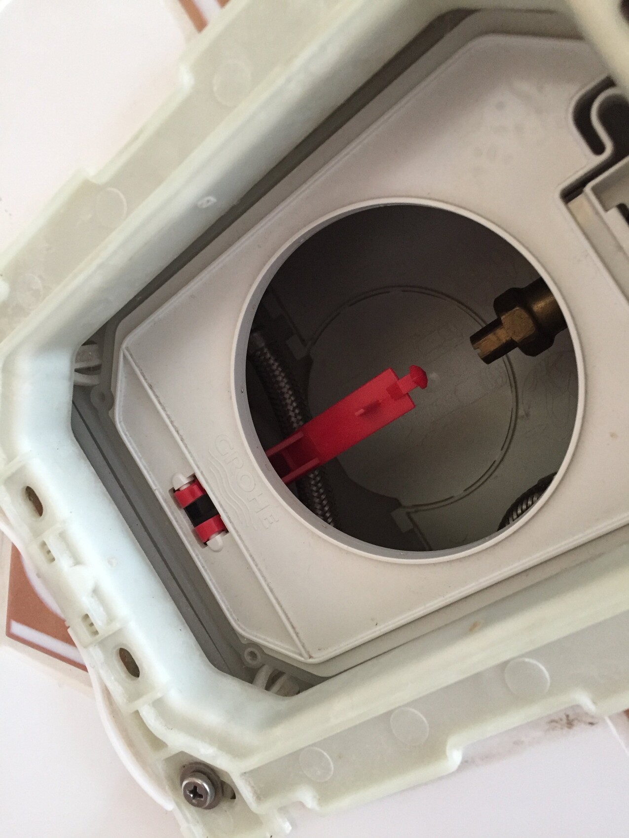 Blick in eine Sanitärinstallation: rundes Öffnungsloch mit rotem Stift und GROHE-Teile