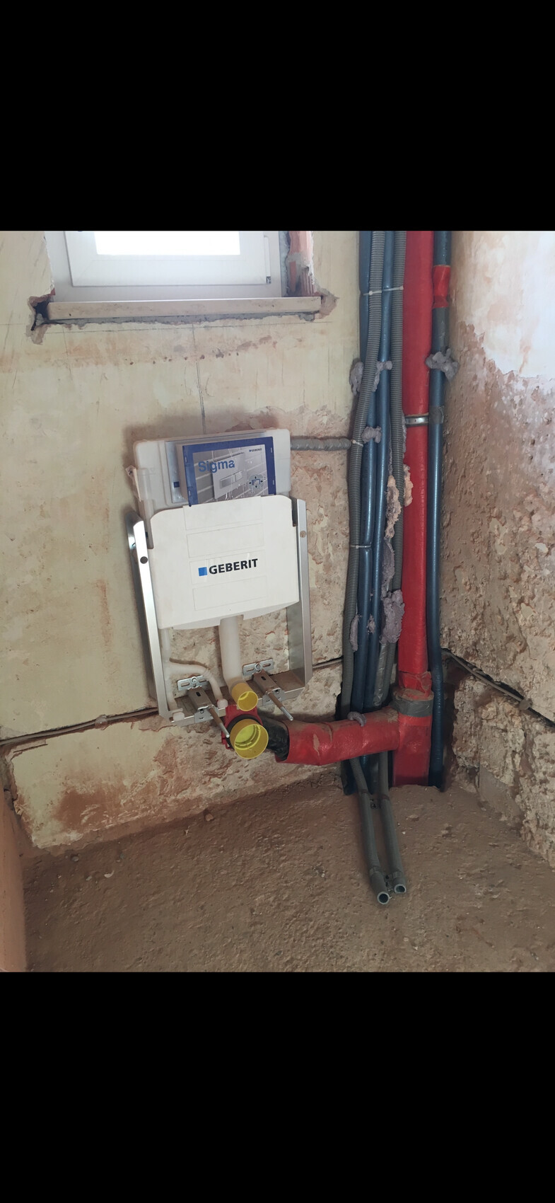 Geberit Sigma Spülkasten an einer Rohbauwand, rote und blaue Wasserleitungen sichtbar.