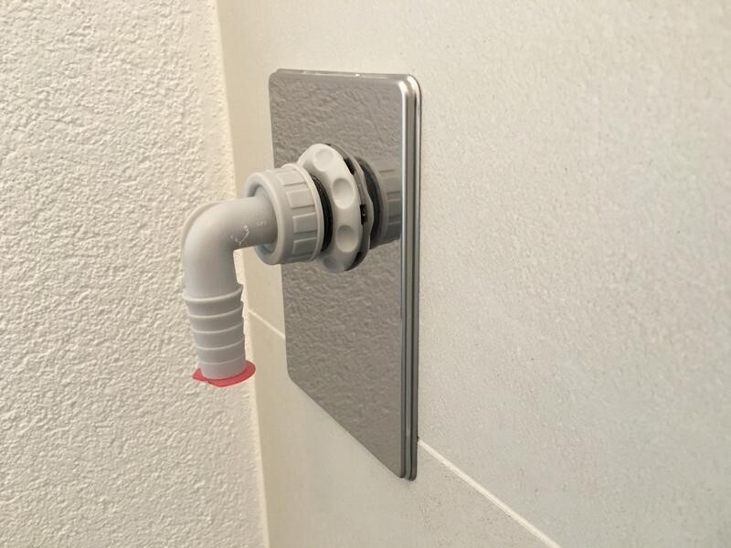 Weißer Kunststoff-Rohrbogen mit Dichtung, vor glänzender Metall-Wandplatte montiert.