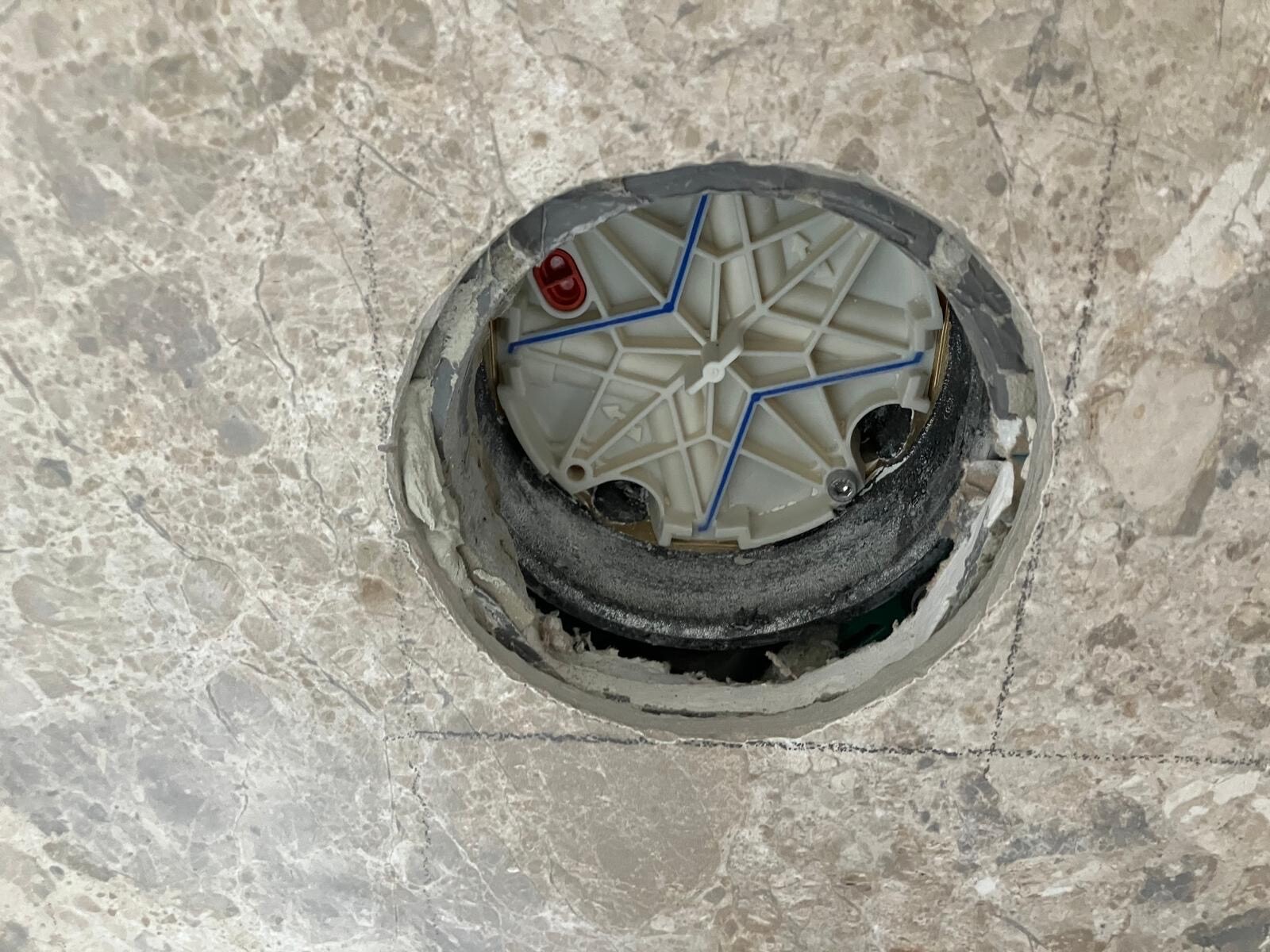 Bodenöffnung mit Sanitärinstallationskörper im unfertigen Estrich, blaue Leitungen sichtbar