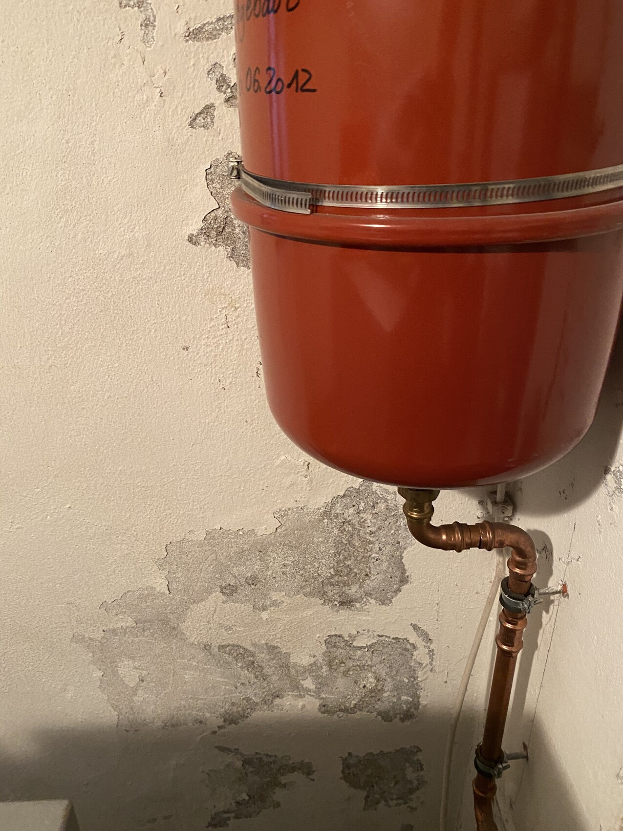 Roter Heizungs-Ausdehnungsbehälter an einer Wand, unten Kupferrohrverbindung und abblätternder Putz.