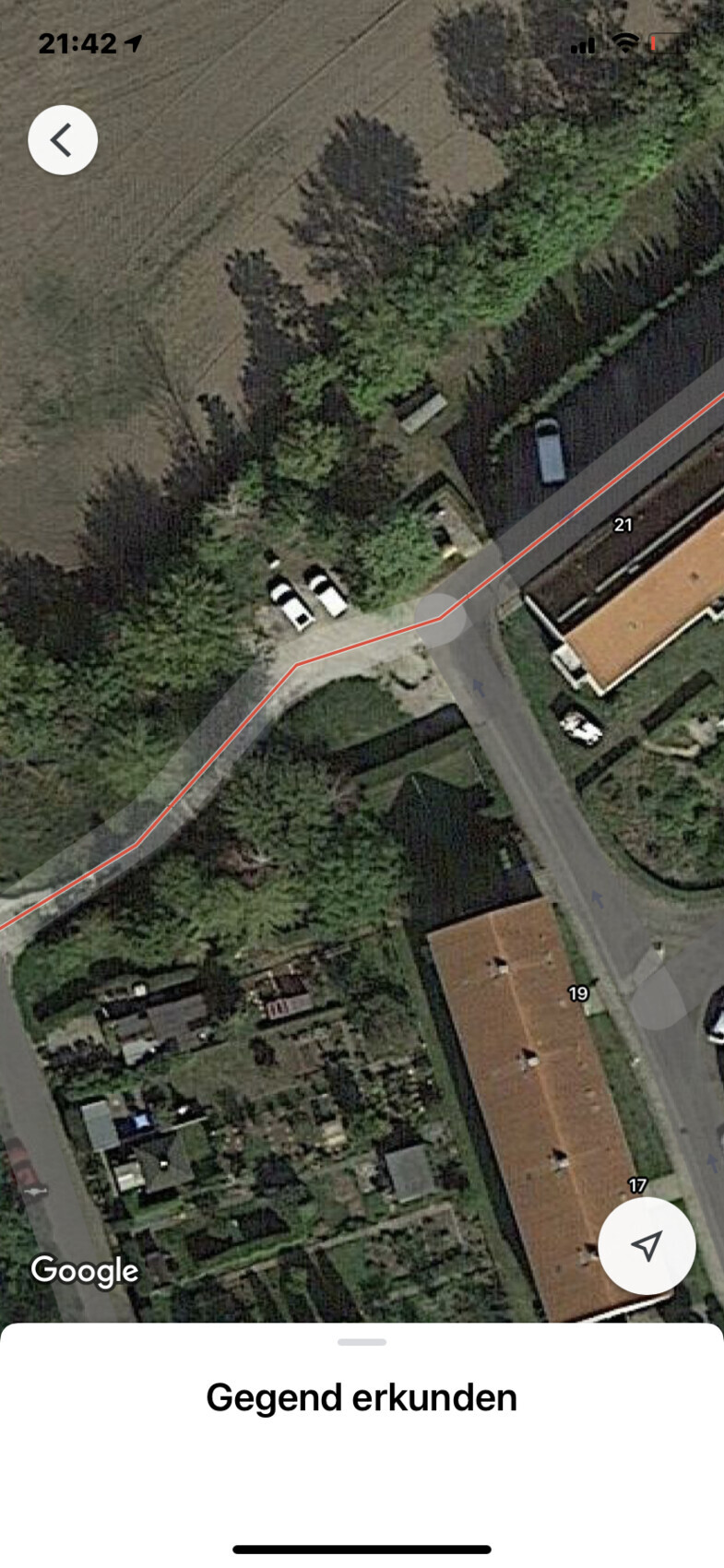 Luftbild eines Wohngebiets: Kurvige Straße, rote Routenlinie, geparkte Autos, Häuser und Gärten.