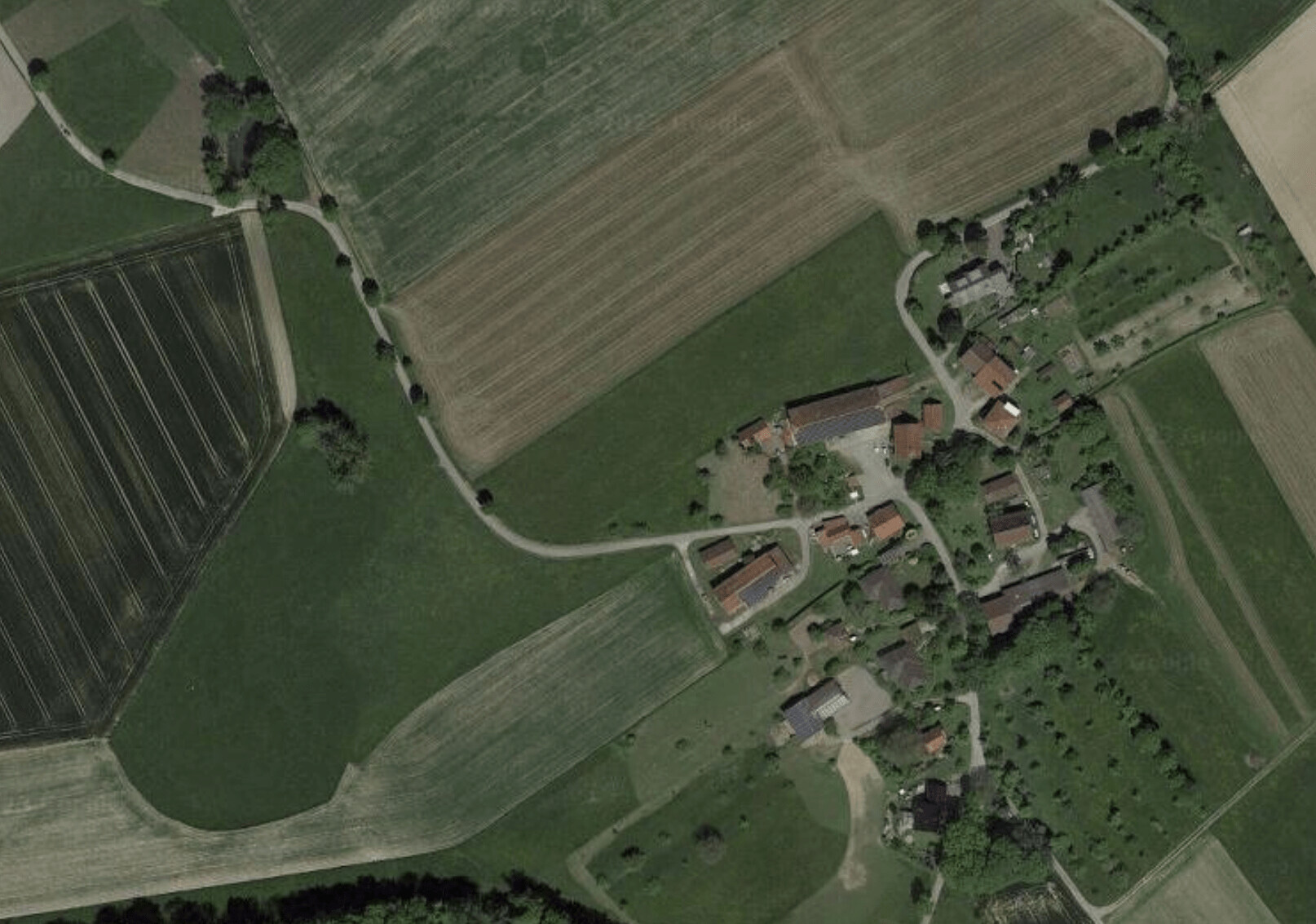 Luftaufnahme eines kleinen Dorfes mit Feldern, Wiesen und Straßen aus der Vogelperspektive.