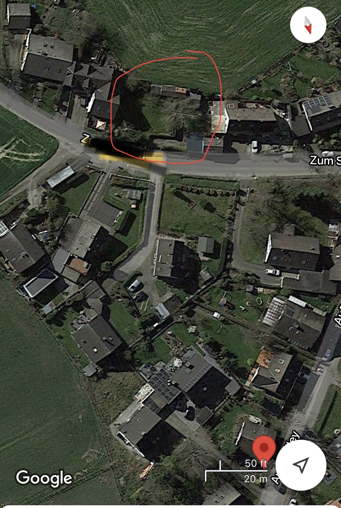 Satellitenbild einer Wohnsiedlung: Ein Haus mit Garten am Straßenrand, umliegende Felder und Nachbarhäuser.