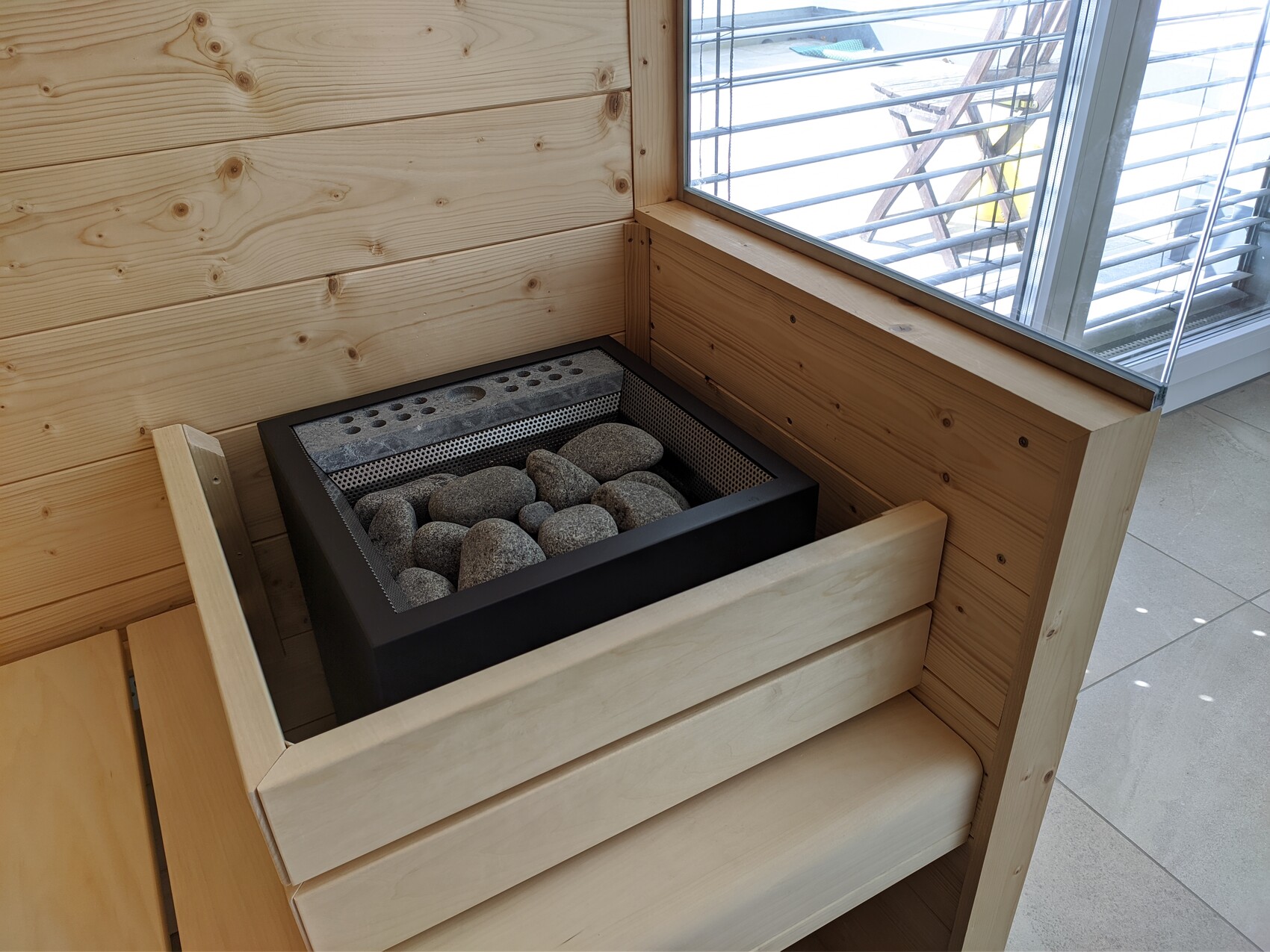 Saunaofen mit sichtbaren Steinen in einer Holzsauna, umgeben von Bänken