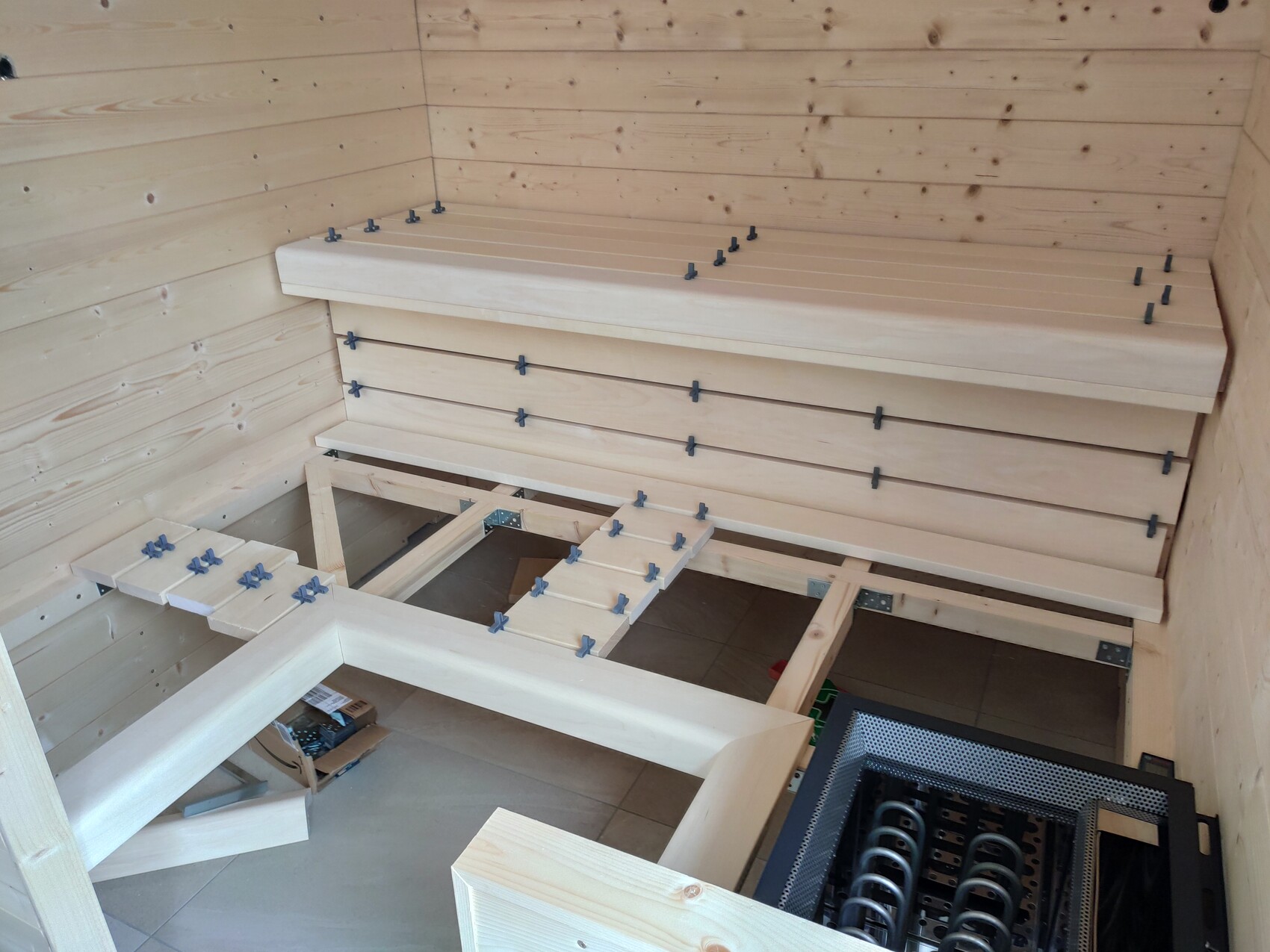 Sauna-Bau: Innenraum mit hellen Holzbänken, Holzverkleidung und Heizgerät unten rechts.