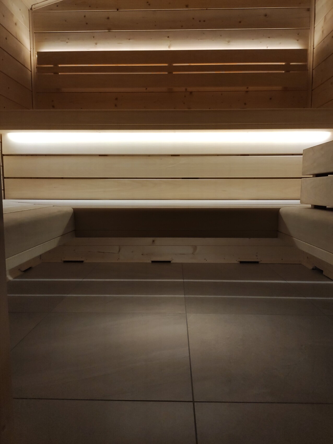Sauna-Innenraum mit Holzbänken, warmem Licht, Holzwänden und Fliesenboden.
