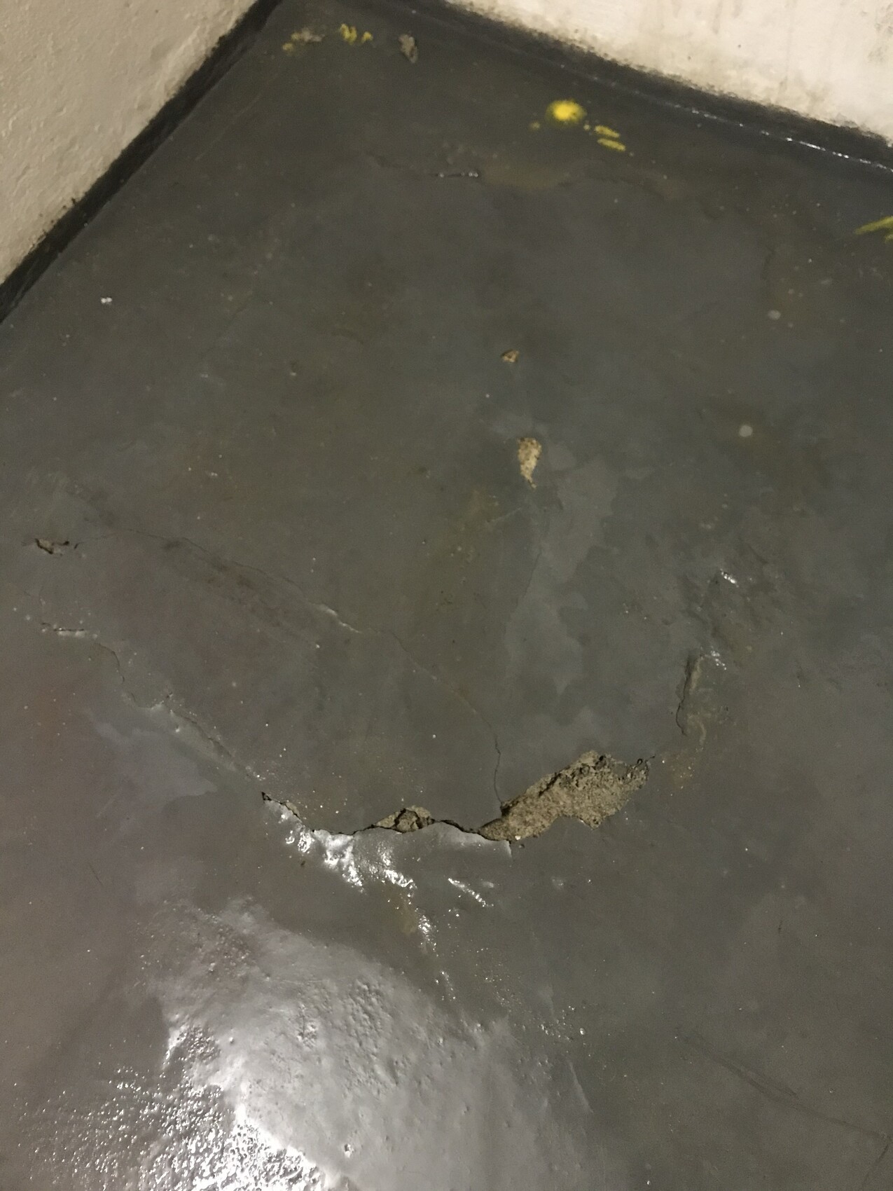 Dunkler Betonboden mit einem großen Riss und freigelegtem Loch nahe der Wand.