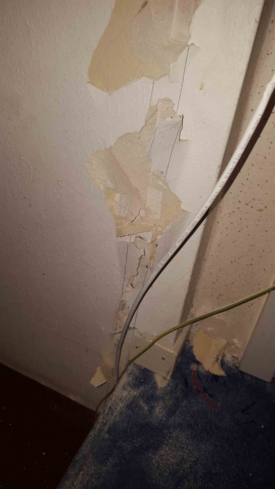 Schadhafter Putz an Wand mit abblätternden Stücken und Kabeln