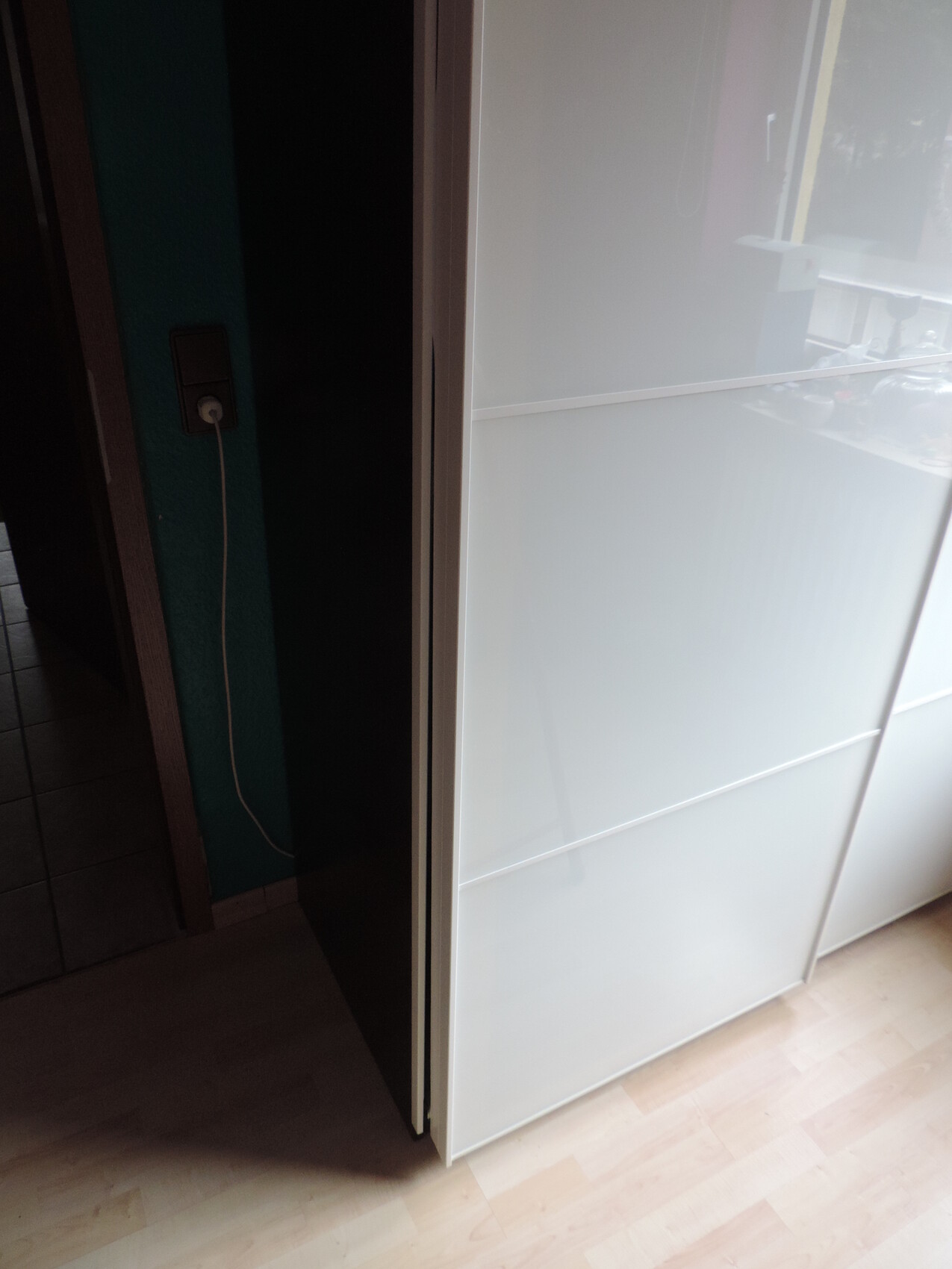 Weiße Milchglas-Schiebetüren eines Schranks neben einer dunklen Wand mit Steckdose und Kabel.