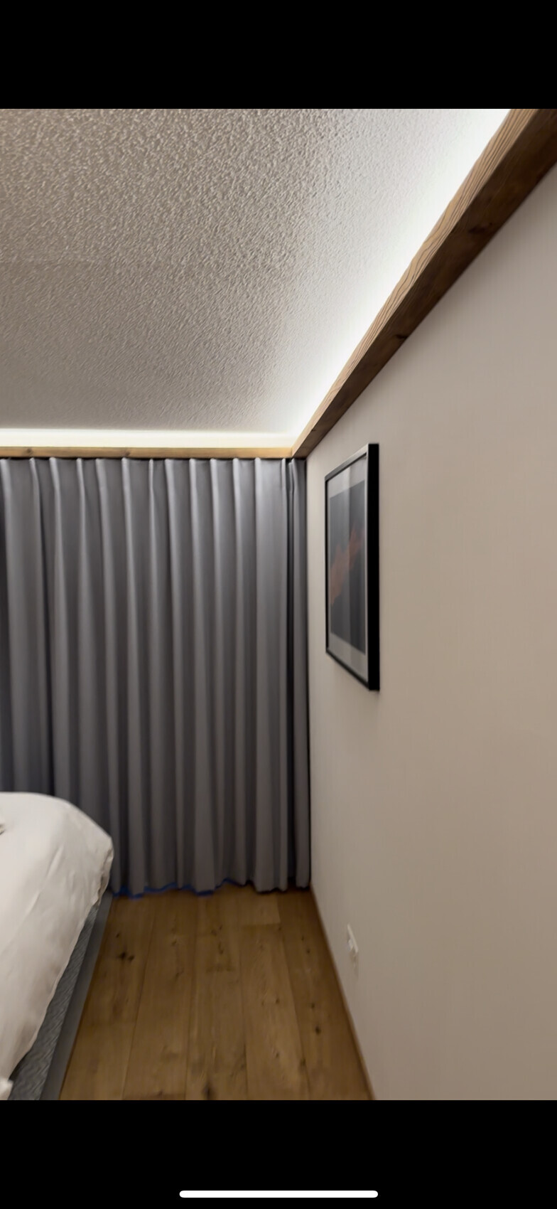 Schlafzimmer-Ecke mit grauen Vorhängen, gerahmtem Bild an der Wand und Holzfußboden.