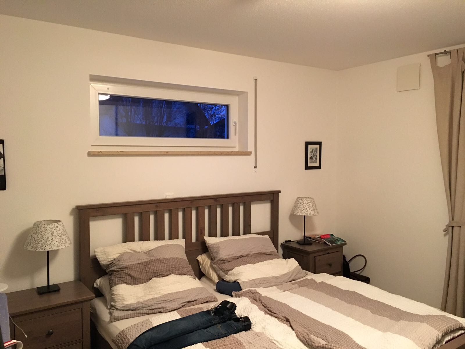 Schlafzimmer mit Holzbett, Nachttischenlampen, neutraler Bettbezug und Fenster.